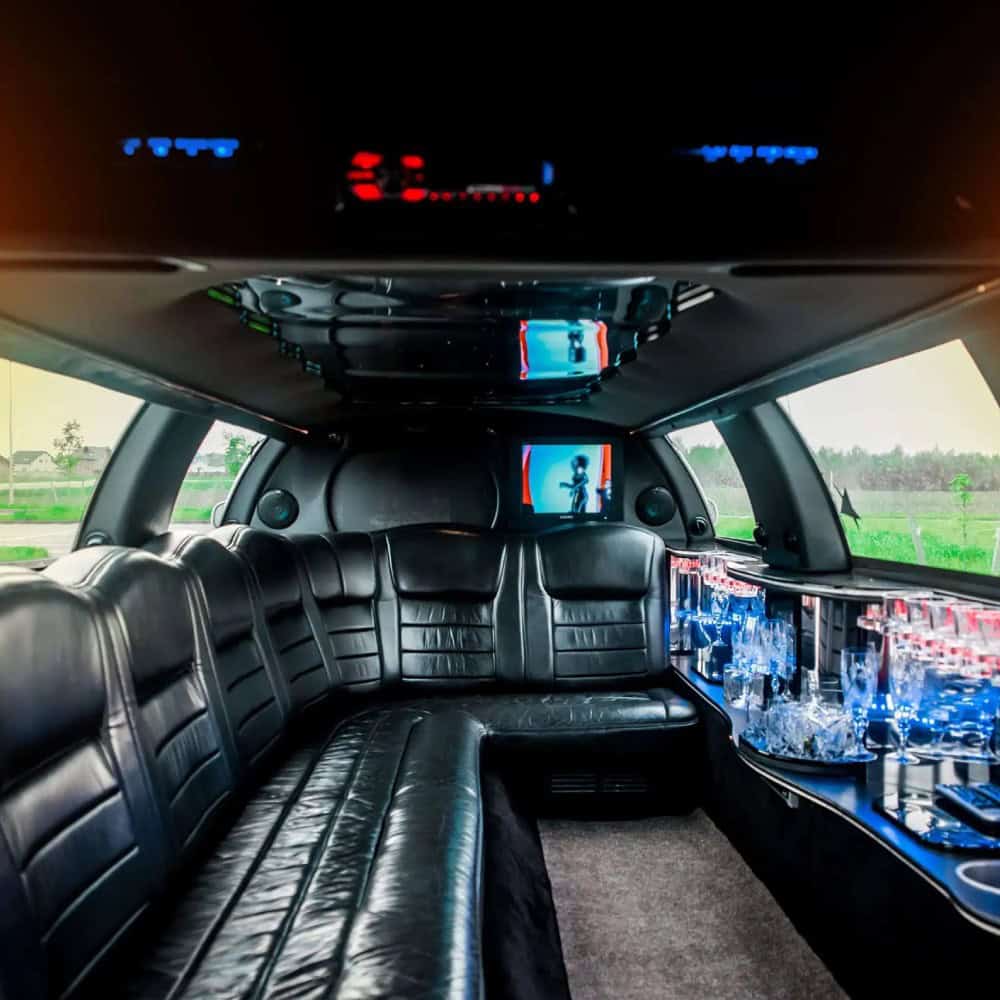 Luxury type of limousine interior with black leather seating, ambient lighting, entertainment screens, and beverage setup for premium chauffeur transportation.